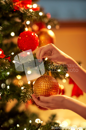 Image of hands decorating christmas tree with ball