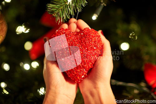 Image of hands decorating christmas tree with red heart