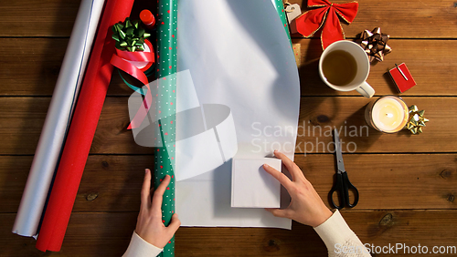 Image of hands wrapping christmas gift into paper at home