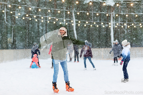 Image of happy young man at outdoor skating rink in winter
