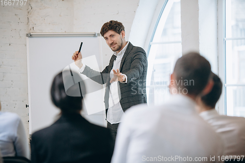 Image of Male speaker giving presentation in hall at workshop. Audience or conference hall. Rear view of unrecognized participants.