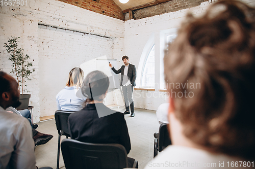 Image of Male speaker giving presentation in hall at workshop. Audience or conference hall. Rear view of unrecognized participants.