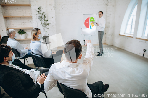 Image of Male speaker giving presentation in hall at workshop. Audience or conference hall. Rear view of unrecognized participants in face masks, Covid.