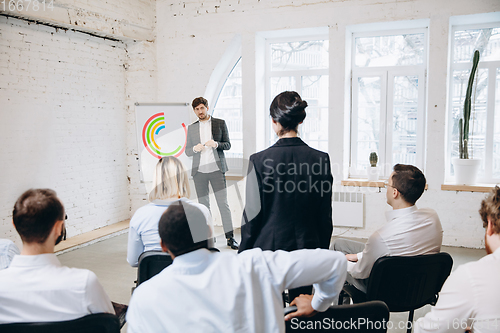 Image of Male speaker giving presentation in hall at workshop. Audience or conference hall. Rear view of unrecognized participants.