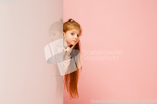 Image of Happy kid, girl isolated on coral pink studio background. Looks happy, cheerful, sincere. Copyspace. Childhood, education, emotions concept