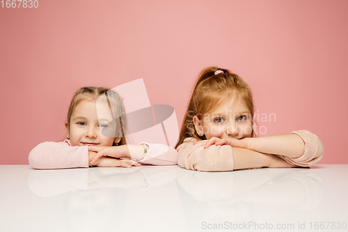 Image of Happy kids, girls isolated on coral pink studio background. Look happy, cheerful, sincere. Copyspace. Childhood, education, emotions concept