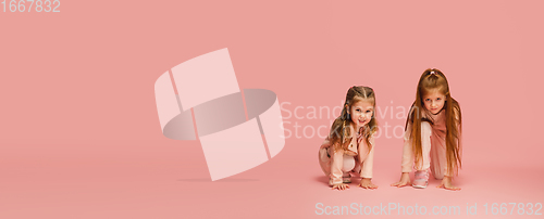 Image of Happy kids, girls isolated on coral pink studio background. Look happy, cheerful, sincere. Copyspace. Childhood, education, emotions concept