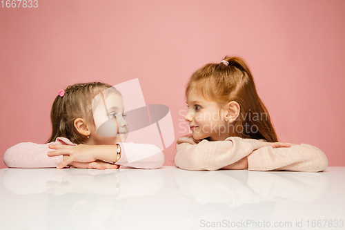 Image of Happy kids, girls isolated on coral pink studio background. Look happy, cheerful, sincere. Copyspace. Childhood, education, emotions concept