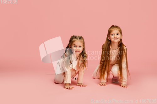 Image of Happy kids, girls isolated on coral pink studio background. Look happy, cheerful, sincere. Copyspace. Childhood, education, emotions concept