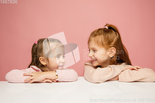 Image of Happy kids, girls isolated on coral pink studio background. Look happy, cheerful, sincere. Copyspace. Childhood, education, emotions concept