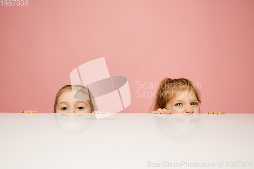 Image of Happy kids, girls isolated on coral pink studio background. Look happy, cheerful, sincere. Copyspace. Childhood, education, emotions concept