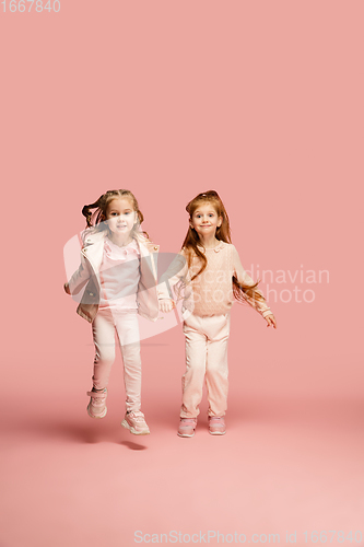 Image of Happy kids, girls isolated on coral pink studio background. Look happy, cheerful, sincere. Copyspace. Childhood, education, emotions concept