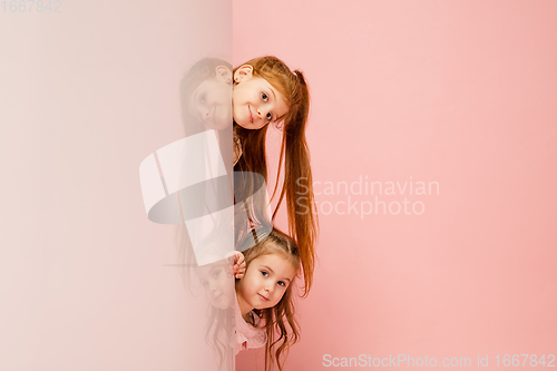 Image of Happy kids, girls isolated on coral pink studio background. Look happy, cheerful, sincere. Copyspace. Childhood, education, emotions concept