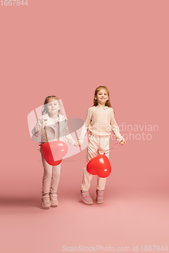 Image of Happy kids, girls isolated on coral pink studio background. Look happy, cheerful, sincere. Copyspace. Childhood, education, emotions concept