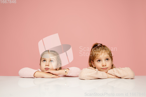 Image of Happy kids, girls isolated on coral pink studio background. Look happy, cheerful, sincere. Copyspace. Childhood, education, emotions concept