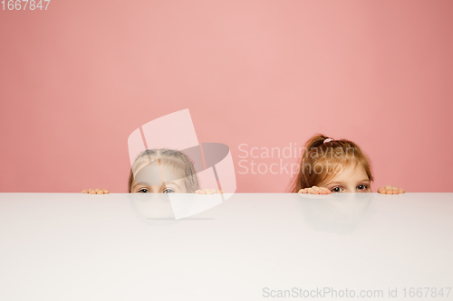 Image of Happy kids, girls isolated on coral pink studio background. Look happy, cheerful, sincere. Copyspace. Childhood, education, emotions concept