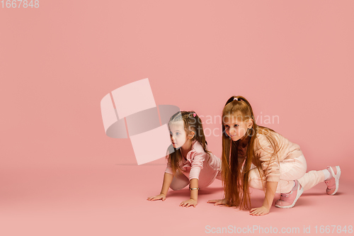 Image of Happy kids, girls isolated on coral pink studio background. Look happy, cheerful, sincere. Copyspace. Childhood, education, emotions concept