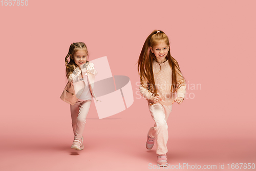 Image of Happy kids, girls isolated on coral pink studio background. Look happy, cheerful, sincere. Copyspace. Childhood, education, emotions concept