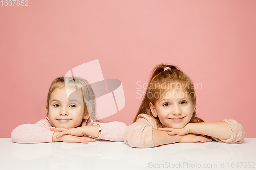 Image of Happy kids, girls isolated on coral pink studio background. Look happy, cheerful, sincere. Copyspace. Childhood, education, emotions concept