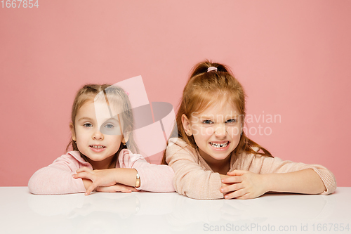 Image of Happy kids, girls isolated on coral pink studio background. Look happy, cheerful, sincere. Copyspace. Childhood, education, emotions concept