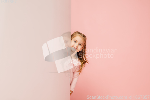 Image of Happy kid, girl isolated on coral pink studio background. Looks happy, cheerful, sincere. Copyspace. Childhood, education, emotions concept