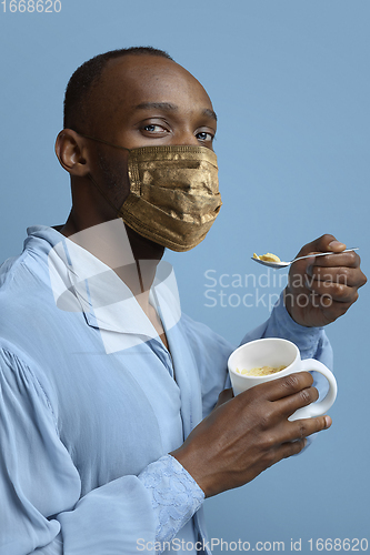 Image of Portrait of medieval young man, grandee in vintage shirt and golden face mask on blue background.