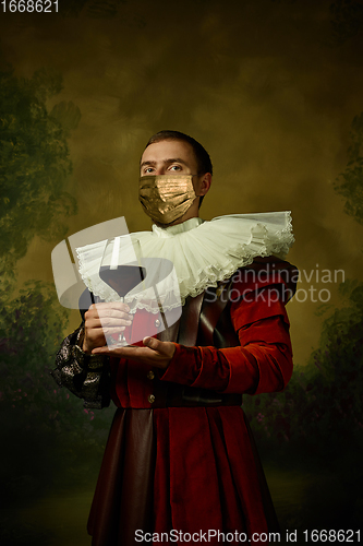 Image of Portrait of medieval young man in vintage clothing and golden face mask standing on dark background.