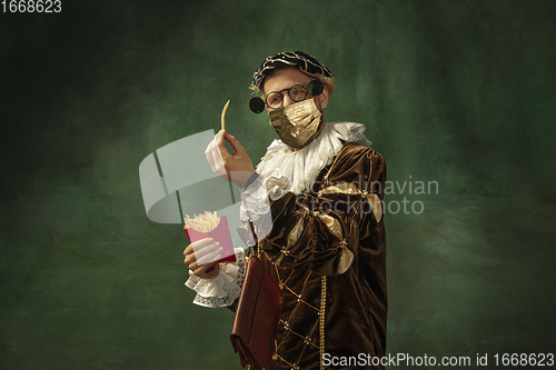 Image of Portrait of medieval young man in vintage clothing and golden face mask standing on dark background.