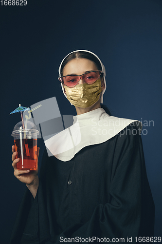 Image of Medieval young woman as a nun in vintage clothing and golden face mask on dark blue background. Concept of comparison of eras, protection from covid