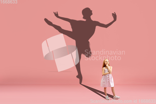 Image of Childhood and dream about big and famous future. Conceptual image with girl and shadow of fit ballerina dancing on coral pink background