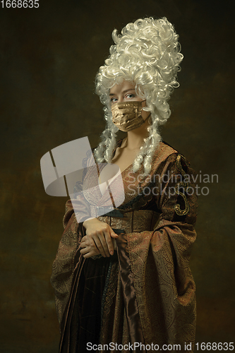 Image of Portrait of medieval young woman in vintage clothes and golden face mask on dark background.