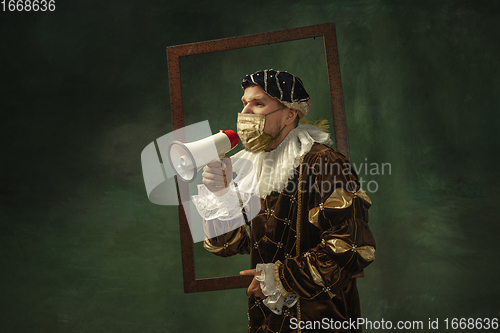 Image of Portrait of medieval young man in vintage clothing and golden face mask standing on dark background.