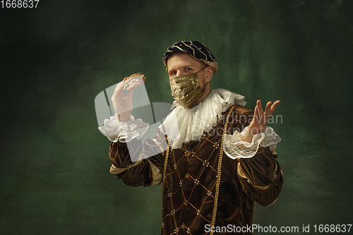 Image of Portrait of medieval young man in vintage clothing and golden face mask standing on dark background.