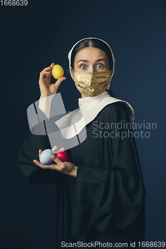 Image of Medieval young woman as a nun in vintage clothing and golden face mask on dark blue background. Concept of comparison of eras, protection from covid