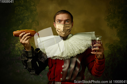 Image of Portrait of medieval young man in vintage clothing and golden face mask standing on dark background.