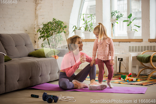 Image of Young woman exercising fitness, aerobic, yoga at home, sporty lifestyle. Getting active while child, daughter playing with her, home gym.