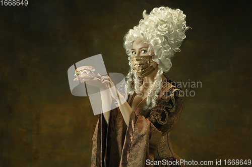 Image of Portrait of medieval young woman in vintage clothes and golden face mask on dark background.