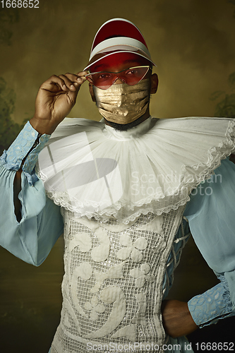 Image of Portrait of medieval young man in vintage clothing and golden face mask on dark background.