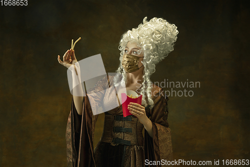 Image of Portrait of medieval young woman in vintage clothes and golden face mask on dark background.