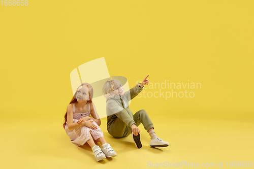 Image of Childhood and dream about big and famous future. Boy and girl isolated on yellow studio background