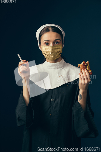 Image of Medieval young woman as a nun in vintage clothing and golden face mask on dark blue background. Concept of comparison of eras, protection from covid