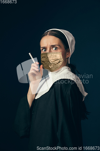 Image of Medieval young woman as a nun in vintage clothing and golden face mask on dark blue background. Concept of comparison of eras, protection from covid
