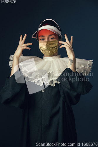 Image of Medieval young woman as a nun in vintage clothing and golden face mask on dark blue background. Concept of comparison of eras, protection from covid