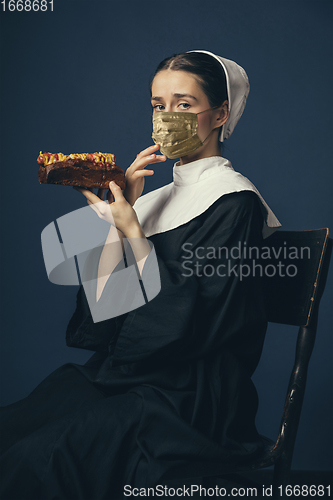 Image of Medieval young woman as a nun in vintage clothing and golden face mask on dark blue background. Concept of comparison of eras, protection from covid