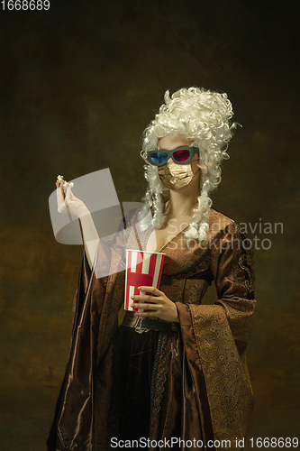 Image of Portrait of medieval young woman in vintage clothes and golden face mask on dark background.