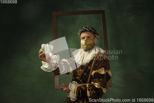 Image of Portrait of medieval young man in vintage clothing and golden face mask standing on dark background.