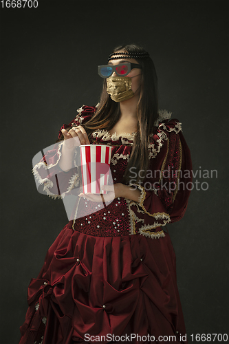 Image of Portrait of medieval young woman in vintage clothes and golden face mask on dark background.