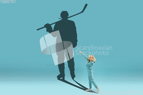Image of Childhood and dream about big and famous future. Conceptual image with boy and shadow of fit male hockey player on blue background
