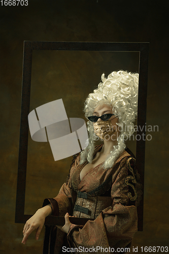 Image of Portrait of medieval young woman in vintage clothes and golden face mask on dark background.