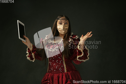 Image of Portrait of medieval young woman in vintage clothes and golden face mask on dark background.